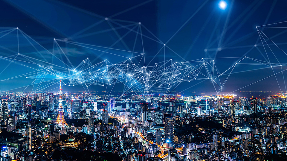 Nighttime city skyline illuminated with lights, overlaid by a digital network of interconnected nodes and lines representing data, communications, or smart city technology.