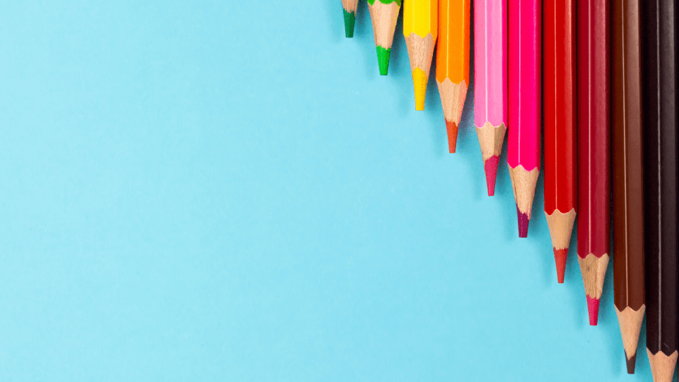 Row of sharpened colored pencils arranged along the top right edge of a light blue background.